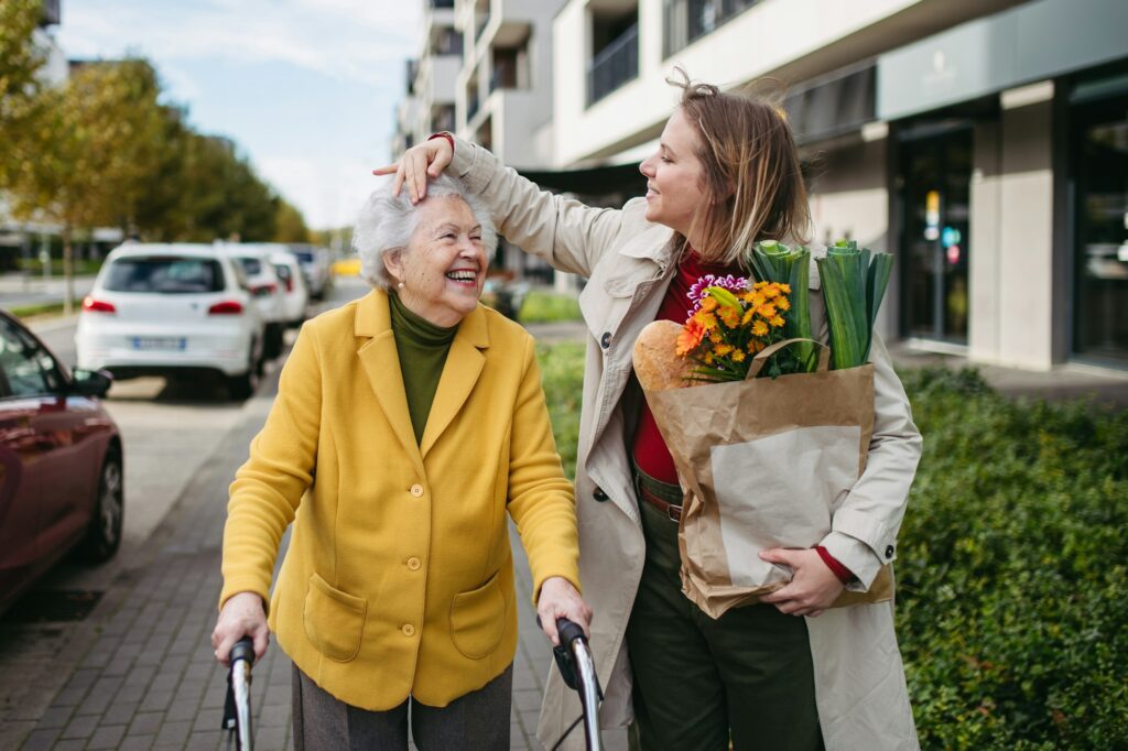 Mature granddaughter carrying grandmother's shopping bag. Senior woman and caregiver going to home